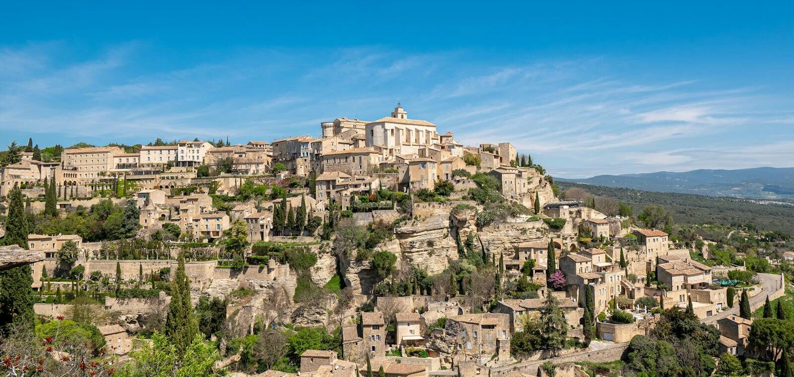 Vue panoramique du village de Gordes perché sur son promontoire rocheux sous un soleil de Provence