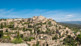 Vue panoramique du village de Gordes perché sur son promontoire rocheux sous un soleil de Provence