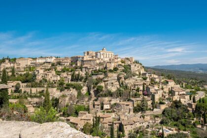 Vue panoramique du village de Gordes perché sur son promontoire rocheux sous un soleil de Provence