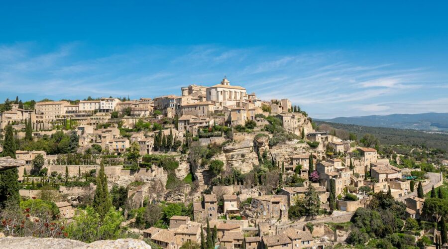 Vue panoramique du village de Gordes perché sur son promontoire rocheux sous un soleil de Provence