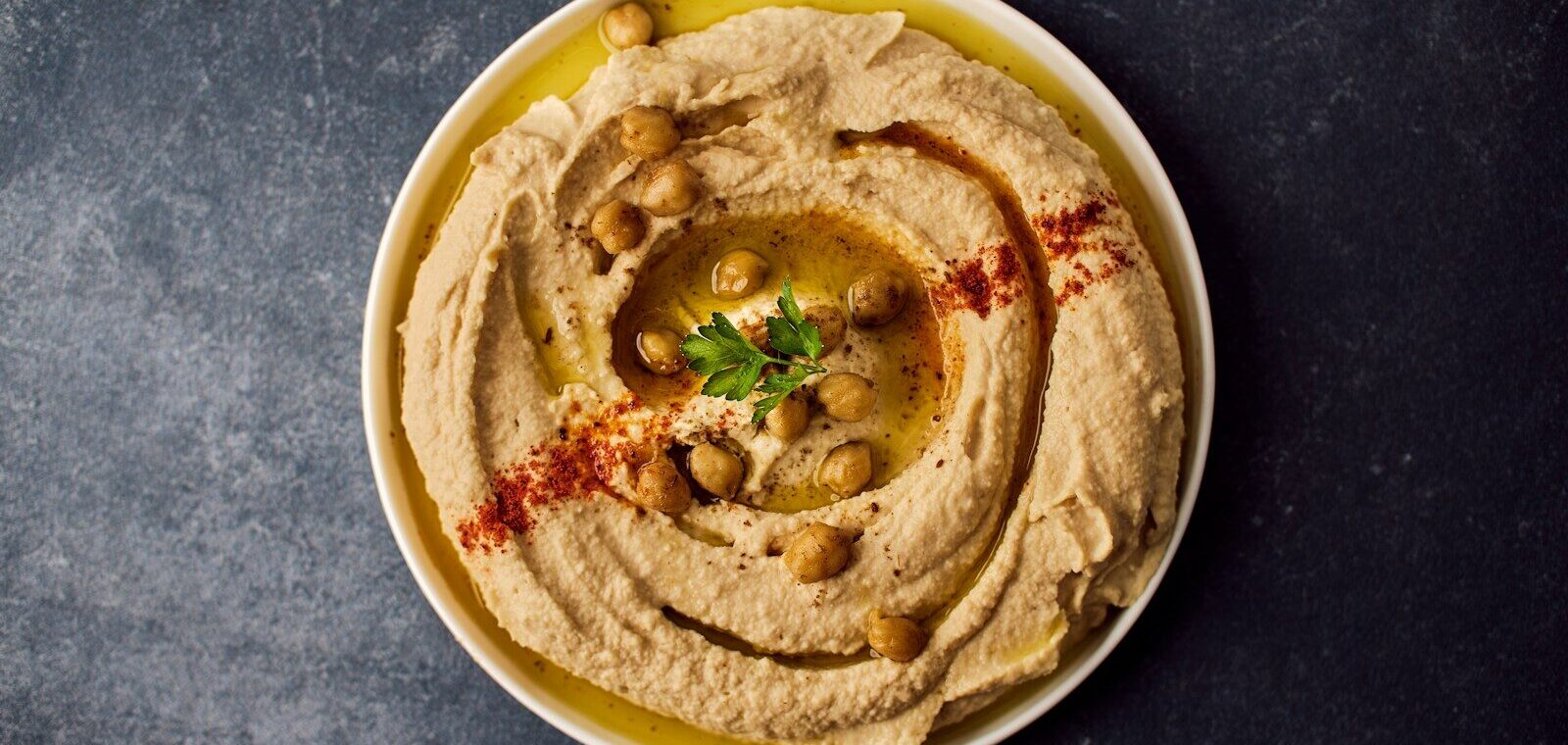 Assiette de houmous maison traditionnel et crémeux, dressé en spirale avec de l'huile d'olive, du paprika et des pois chiches entiers.