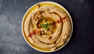 Assiette de houmous maison traditionnel et crémeux, dressé en spirale avec de l'huile d'olive, du paprika et des pois chiches entiers.
