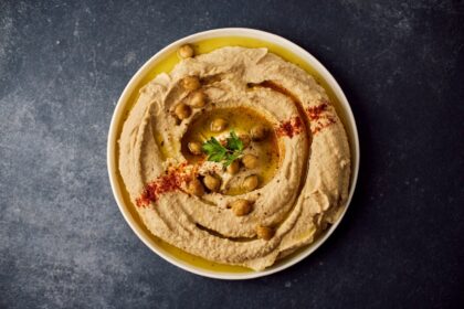 Assiette de houmous maison traditionnel et crémeux, dressé en spirale avec de l'huile d'olive, du paprika et des pois chiches entiers.