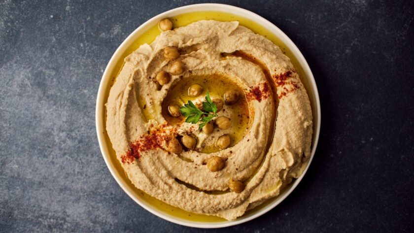 Assiette de houmous maison traditionnel et crémeux, dressé en spirale avec de l'huile d'olive, du paprika et des pois chiches entiers.