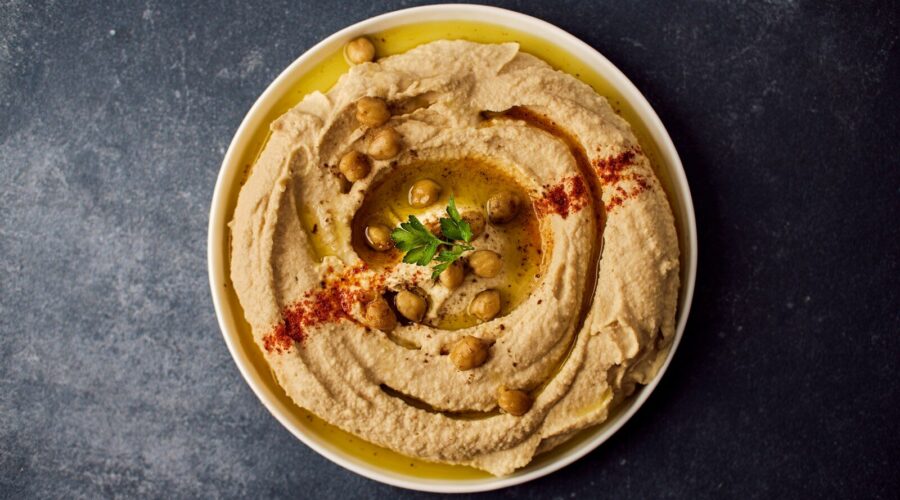 Assiette de houmous maison traditionnel et crémeux, dressé en spirale avec de l'huile d'olive, du paprika et des pois chiches entiers.