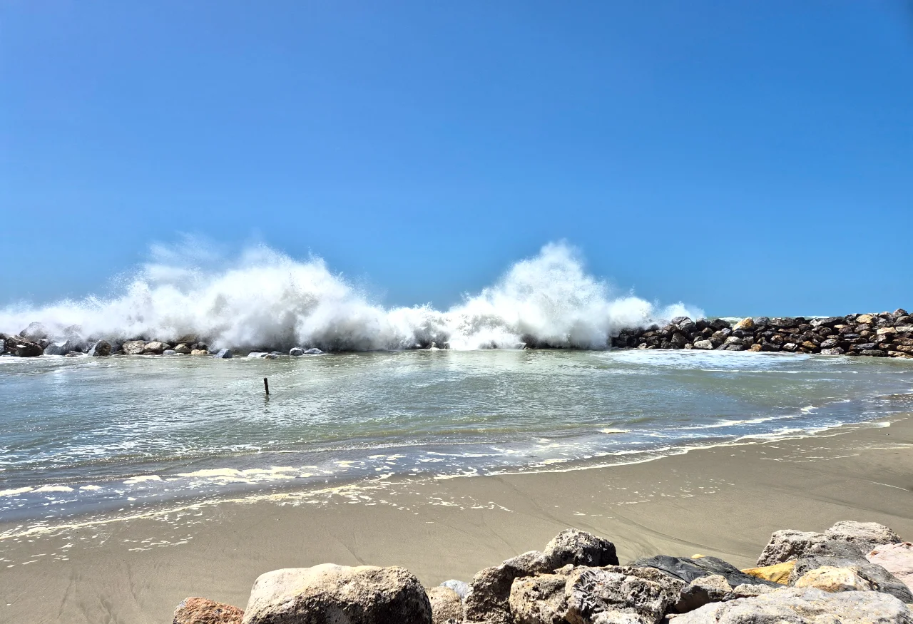Vagues puissantes de la mer Tyrrhénienne se brisant sur les digues de rochers à la Marina di Pisa, littoral toscan sous un ciel bleu azur.