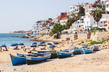 Panorama de la plage principale de Taghazout au Maroc avec ses barques de pêcheurs bleues traditionnelles sur le sable et ses maisons blanches en bord de mer.
