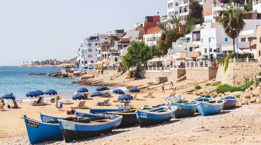 Panorama de la plage principale de Taghazout au Maroc avec ses barques de pêcheurs bleues traditionnelles sur le sable et ses maisons blanches en bord de mer.
